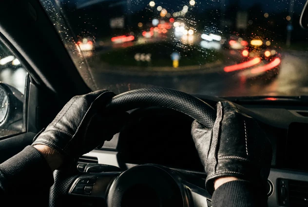 Gros plan sur des mains gantées tenant fermement un volant, symbolisant la concentration et le contrôle nécessaires pour aborder un rond-point.